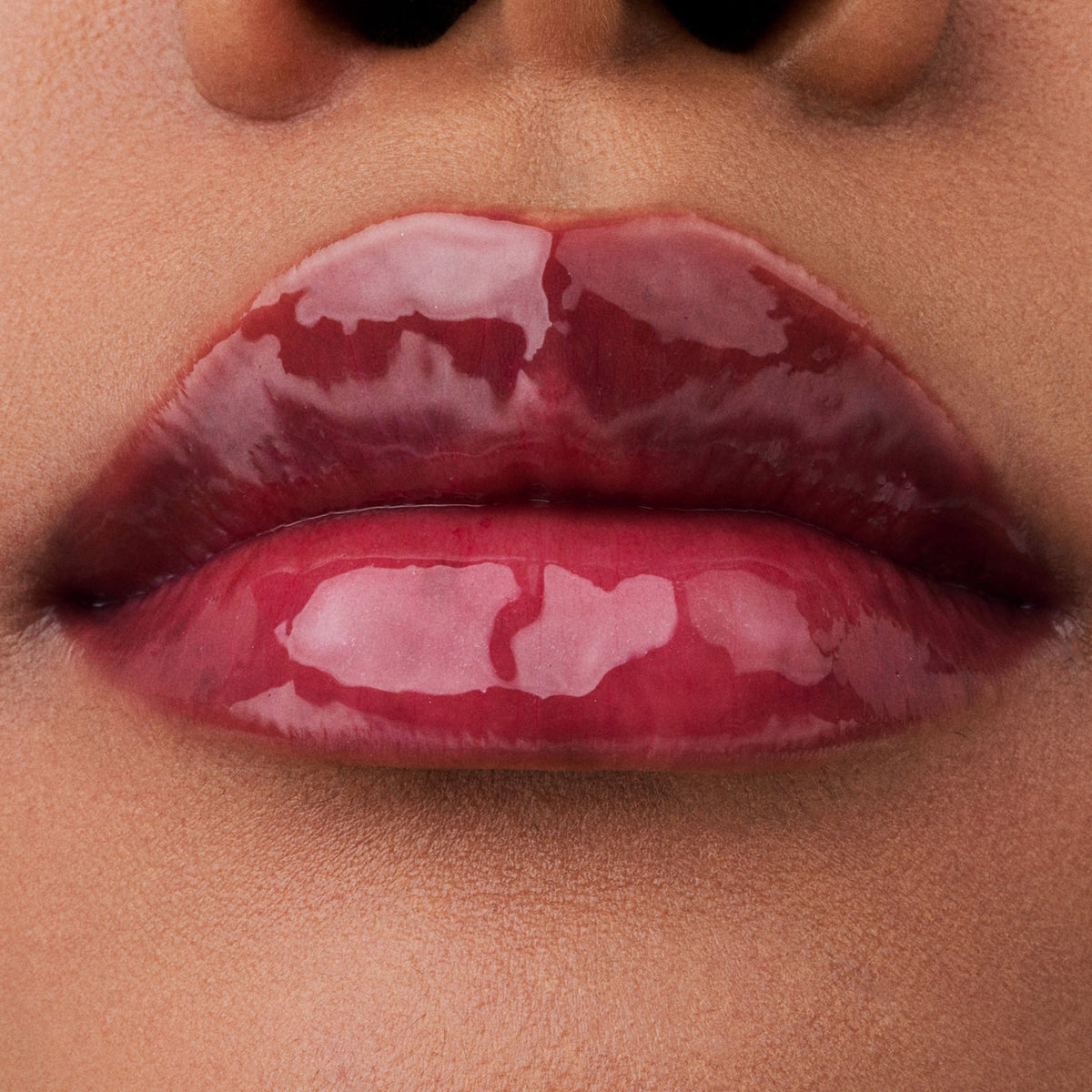 Nahaufnahme der Lippen einer Person mit brauner Haut mit dem Glossin‘ Glow Tinted Lip Oil 010 in glänzendem rosa Farbton.