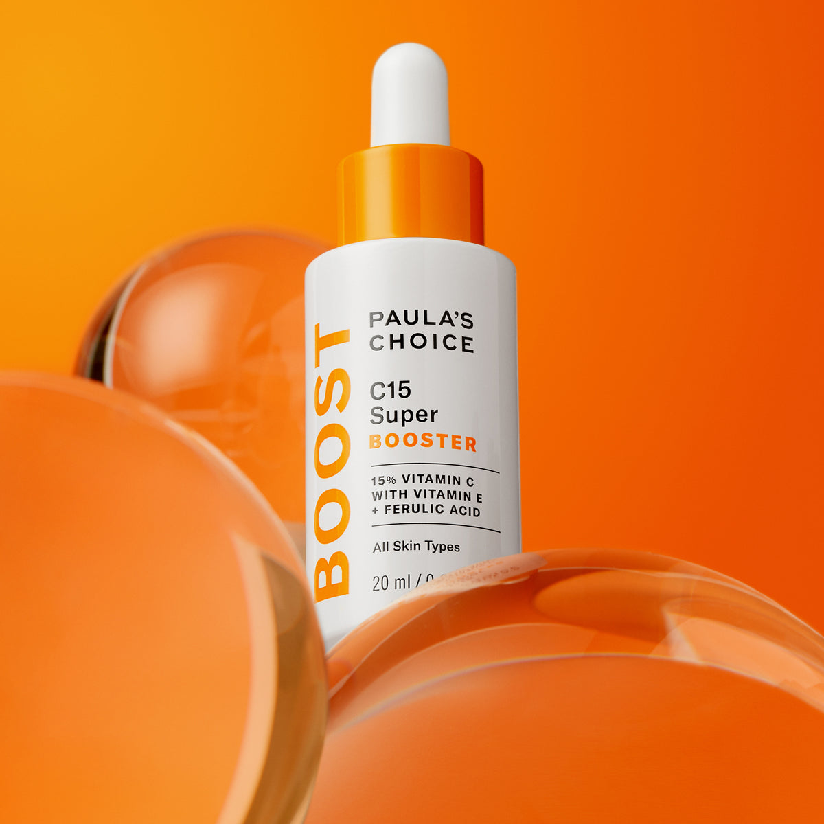 Eine Flasche C15 Super Booster-Serum steht vor einem orangefarbenen Hintergrund mit Glaskugeln.