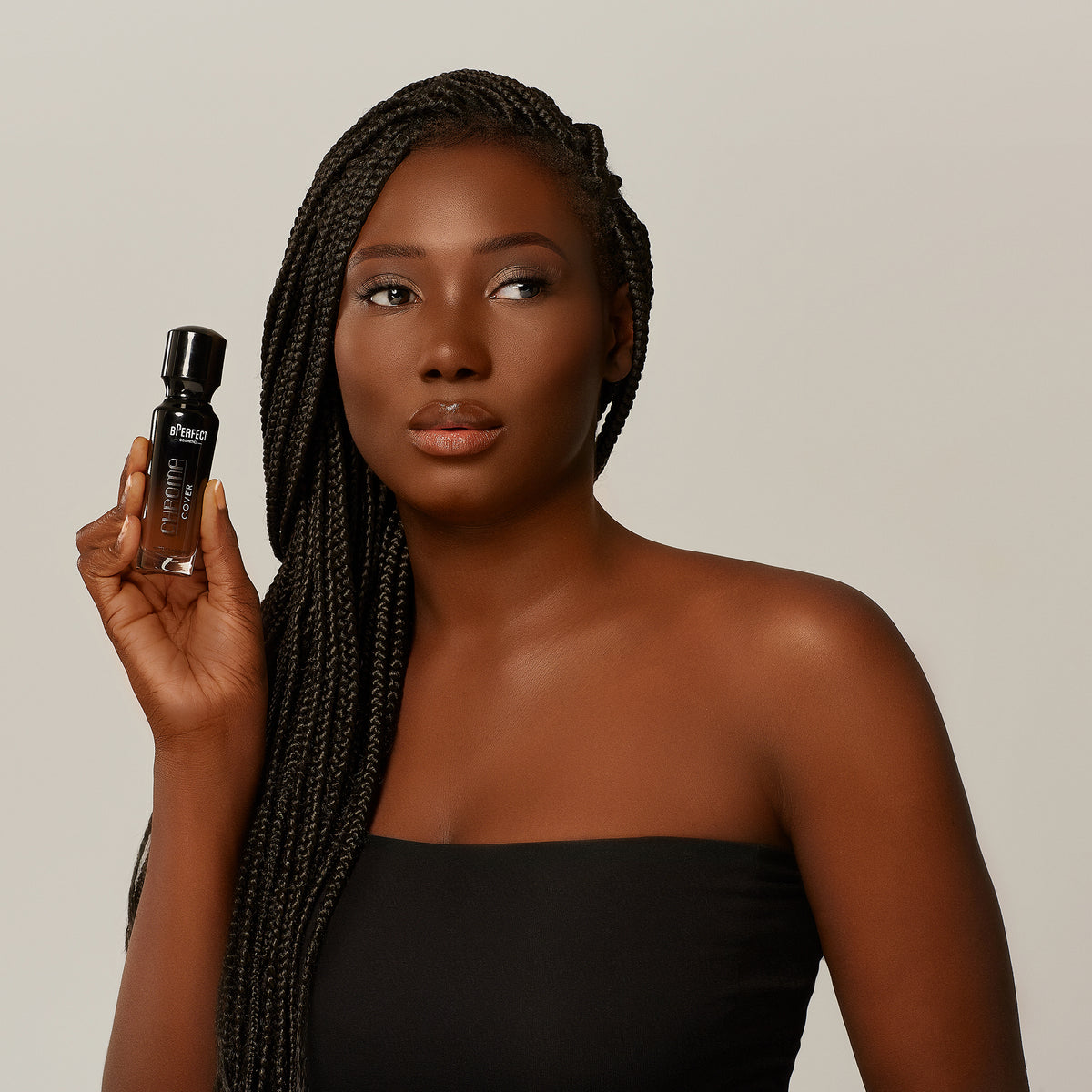 Eine Frau mit dunklem Hautton und schwarzen geflochtenen Haaren hält die Chroma Cover Foundation Matte und blickt zur Seite.