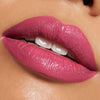 Nahaufnahme von glänzenden rosafarbenen Lippen mit dem Catrice Cosmetics Shine Bomb Lip Lacquer 060, wobei die weißen Zähne leicht zu sehen sind.