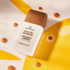 Eine Flasche DROP OF sunshine BRONZING DROPS auf einem leuchtend gelben Hintergrund mit Sonnenmotiv präsentiert.