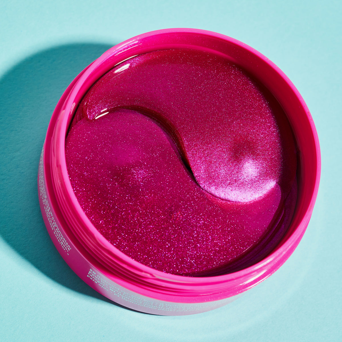 Ein geöffneter rosafarbener Behälter mit pink glitzernden Essence HYDRO GEL Eye Patches (30 Paar) auf einem hellblauen Hintergrund abgebildet.