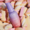 Flasche des Fine Time Pore Minimizer Serums in Lila- und Rosatönen ist von pastellfarbenen Marshmallows umgeben.