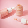 Zwei Flaschen Lumene INVISIBLE ILLUMINATION Illuminizer mit Tropfer auf rosa Hintergrund, eine Flasche geöffnet.