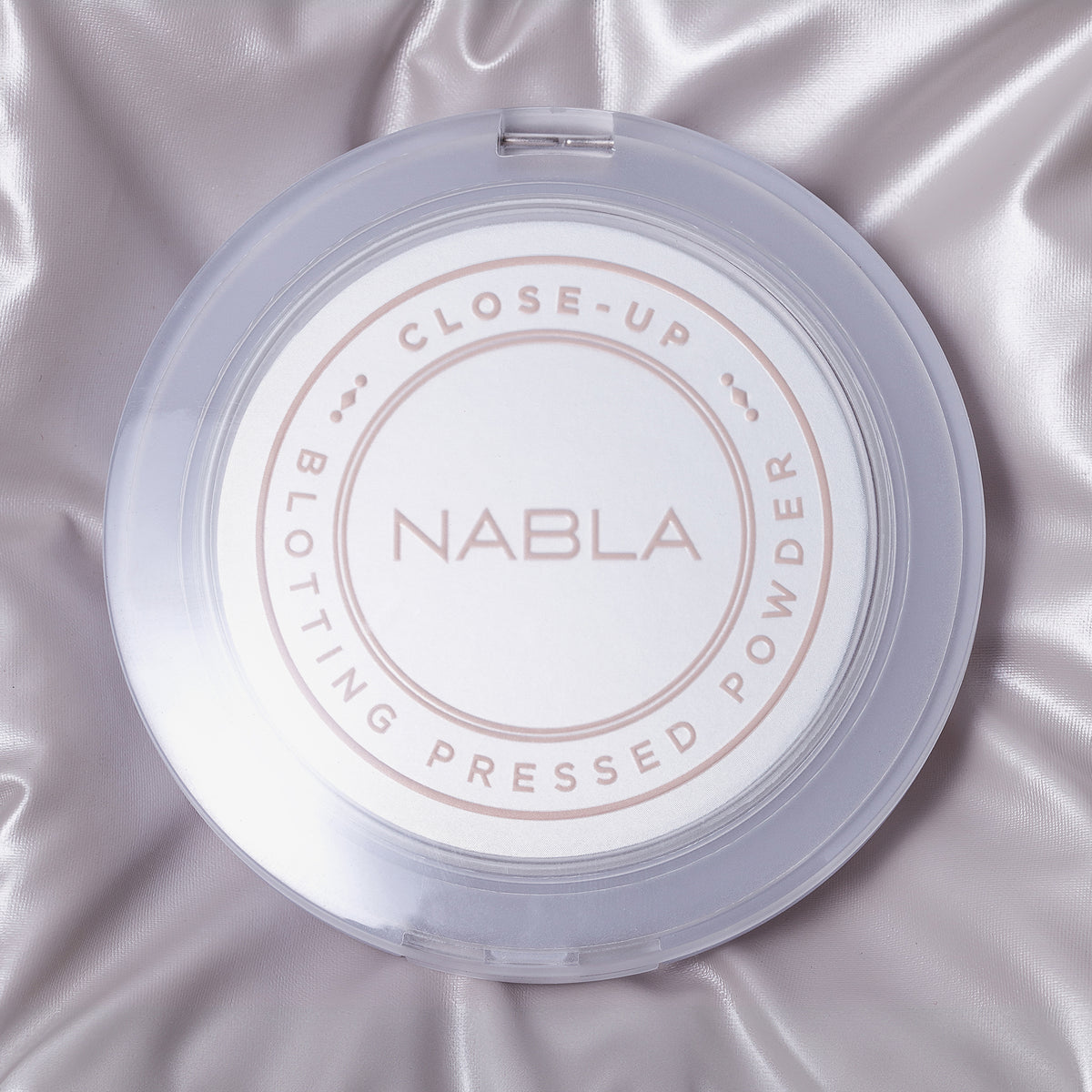 Nahaufnahme von kompaktem Blotting-Puder auf glänzendem, hellviolettem Satinstoff.