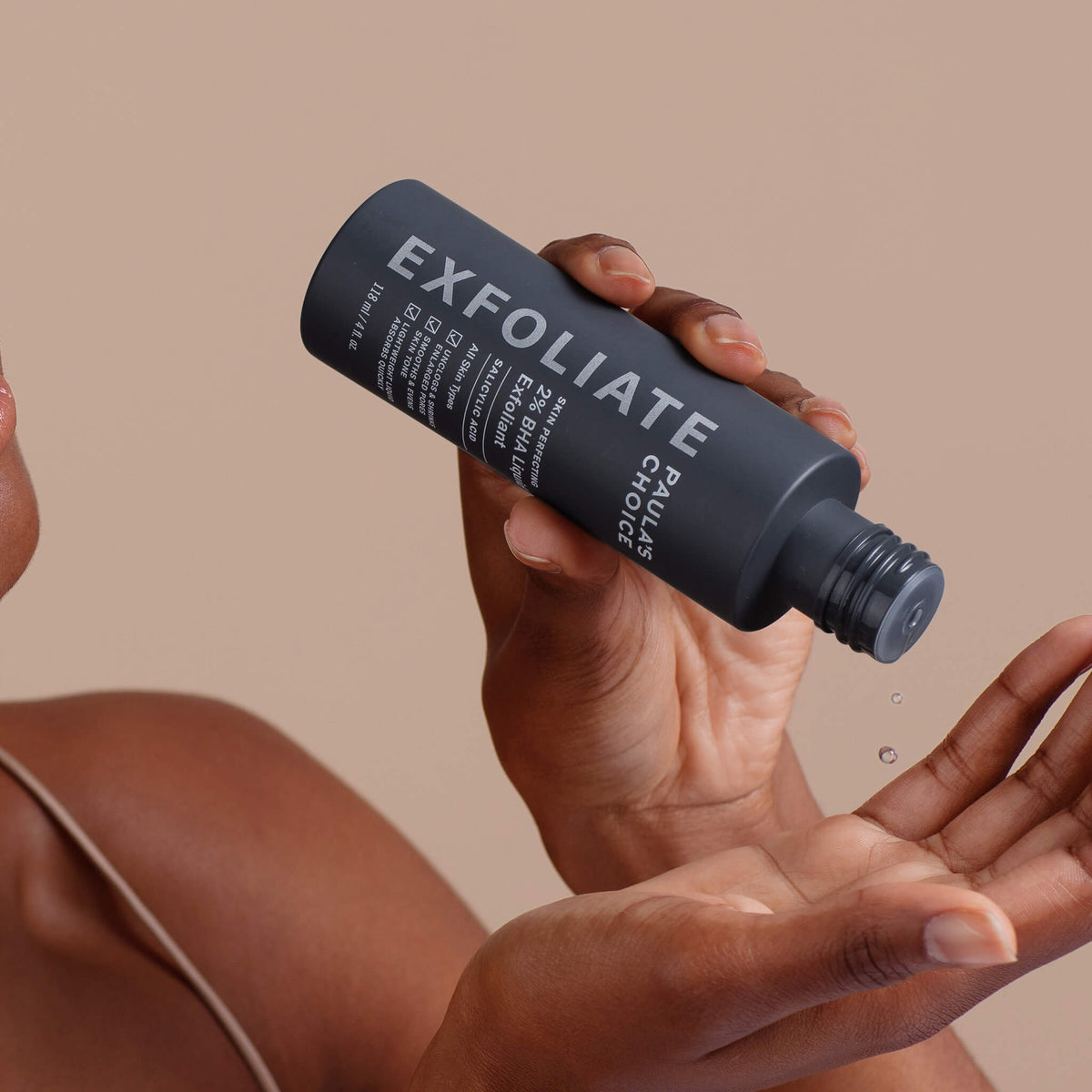 Eine Person gießt das flüssige BHA Peeling aus einer schwarzen Flasche auf ihre Hand.