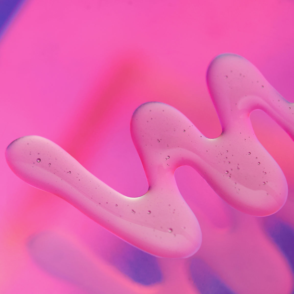 Transparente Geltextur mit feinen Luftbläschen in geschwungener Form auf pink-violettem Hintergrund.
