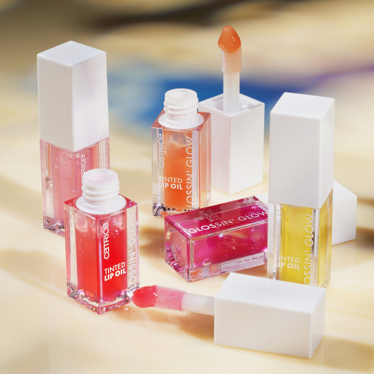 Mehrere Flaschen Glossin‘ Glow Tinted Lip Oil im Freien auf einer hellgelben Oberfläche.