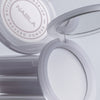 Eine geöffnete Kompaktpackung mit NABLAs Close-up Blotting Pressed Powder gibt den Blick auf einen Spiegel und das darin enthaltene weiße Pulver frei.