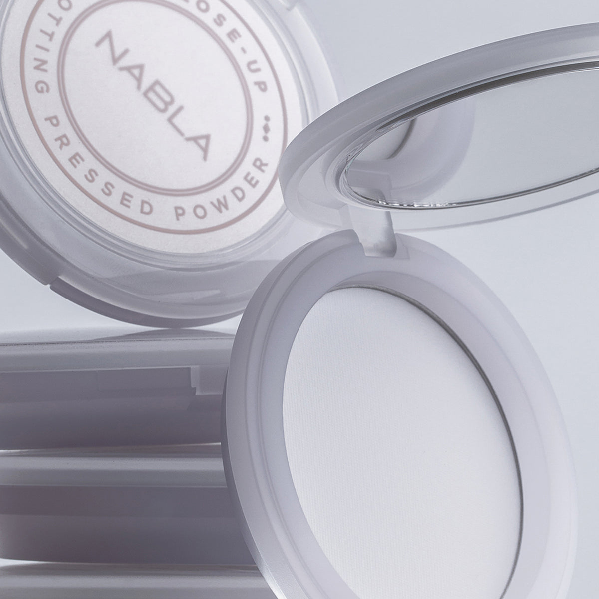 Eine geöffnete Kompaktpackung mit NABLAs Close-up Blotting Pressed Powder gibt den Blick auf einen Spiegel und das darin enthaltene weiße Pulver frei.