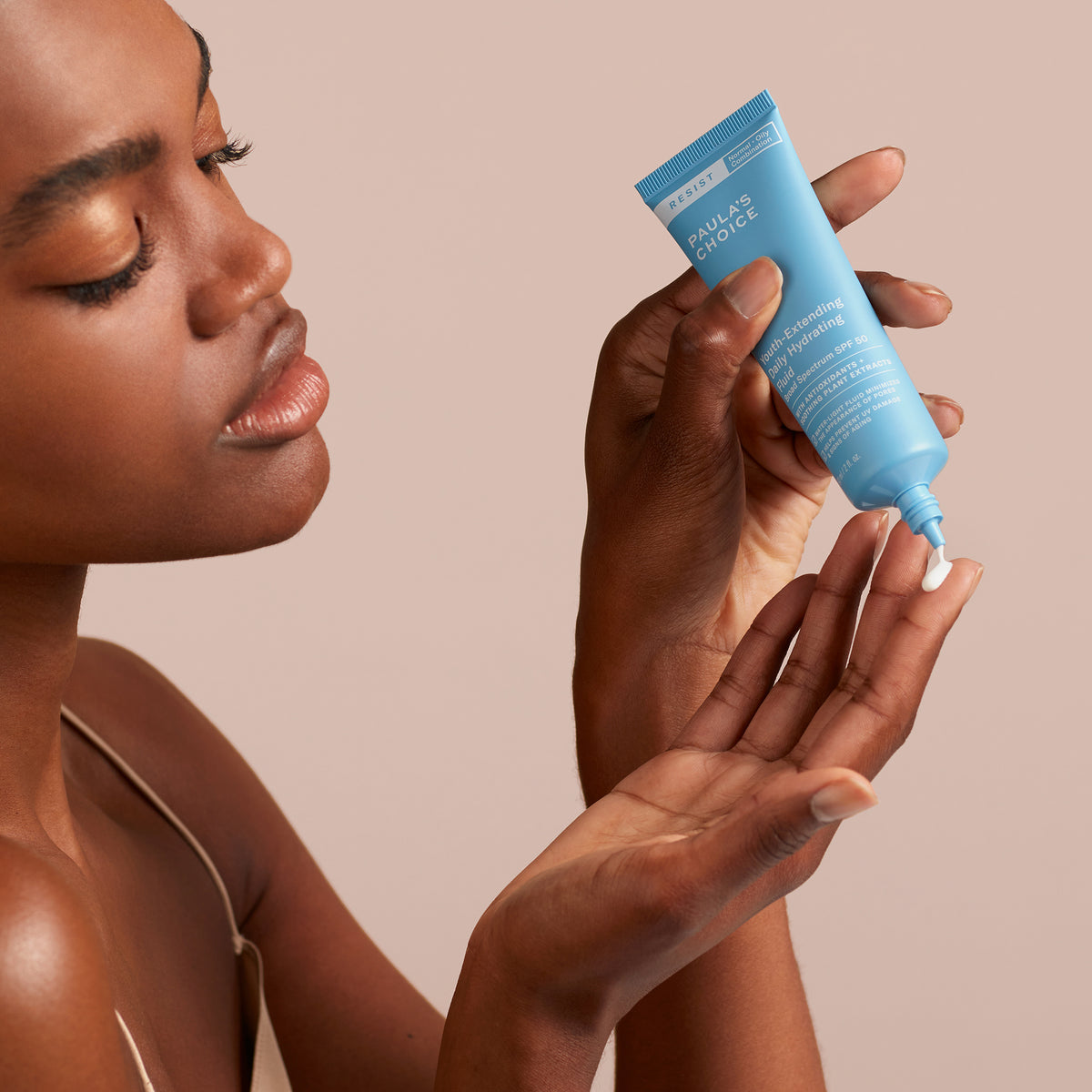 Eine Frau trägt vor einem neutralen Hintergrund das Youth-Extending Daily Hydrating Fluid SPF 50 aus einer blauen Tube auf ihre Fingerspitze auf.