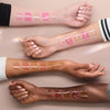 Vier Unterarme unterschiedlicher Hautfarben mit ja 5 Swatches aller erhältlichen Shades des Glossin‘ Glow Tinted Lip Oils