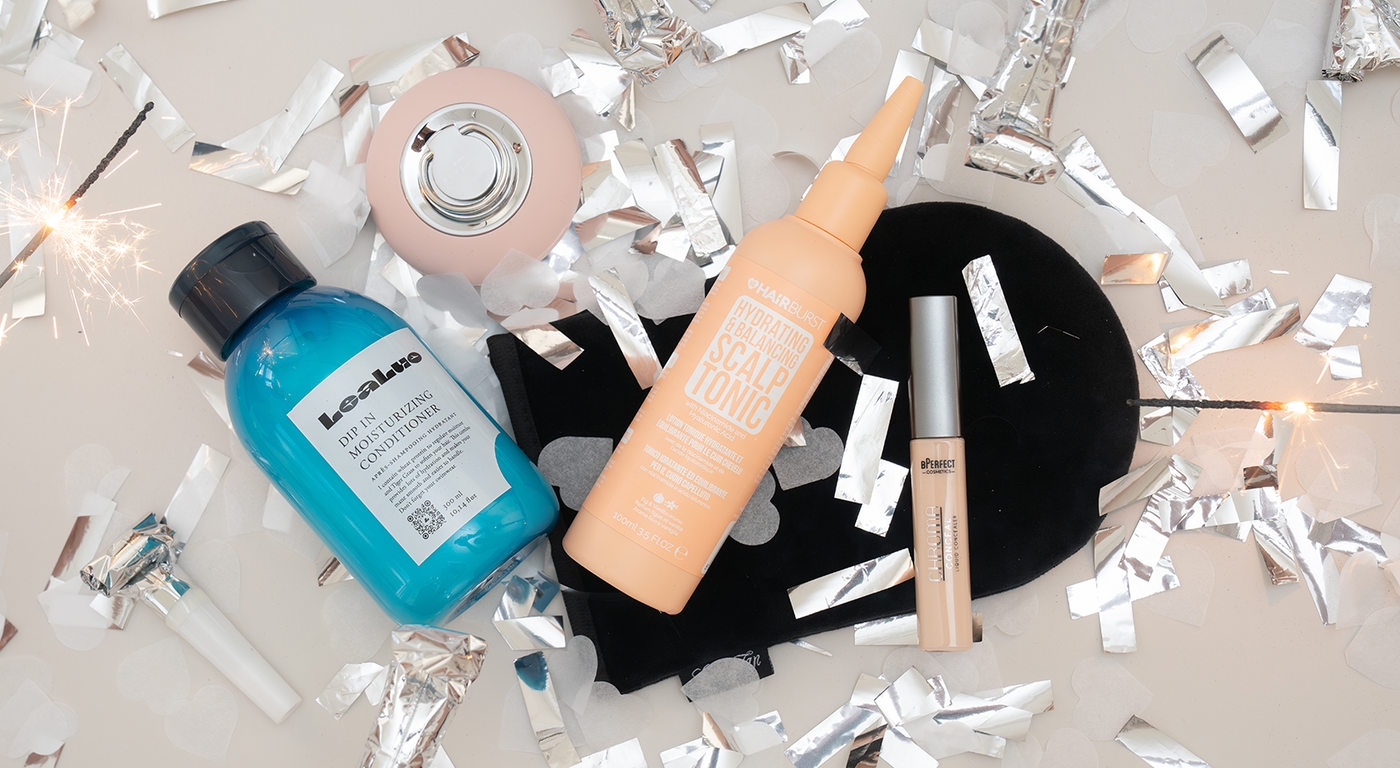 Beautyprodukte von LeaLuo, HAIRBURST und BPerfect auf grauer Oberfläche mit silbernem Konfetti und Wunderkerze.