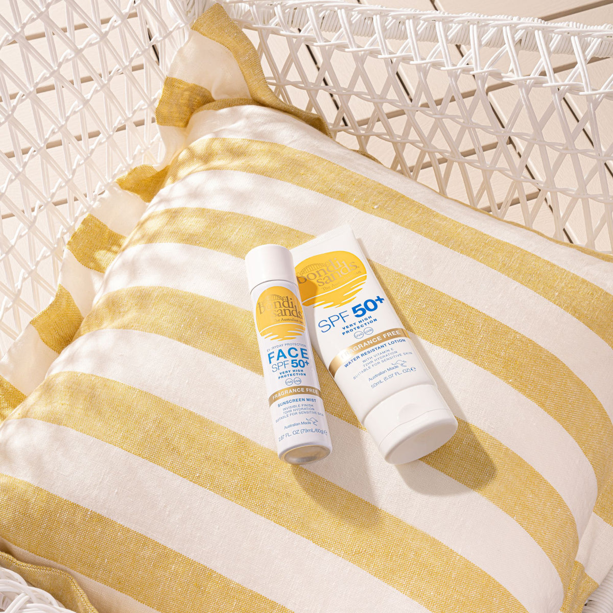 Die SPF50+ Lotion Fragrance Free und die SPF50+ Sunscreen Mist auf einem weiß-gelb gestreiften Kissen.