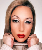 Frau mit auffälligem Make-up, roten Lippen, weißen Strasssteinen um die Augen und hellem Rollkragenpullover.