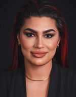 Frau mit starkem Make-up, Lippenpiercing, Augenbrauenpiercings und rotem Haaransatz lächelt leicht in die Kamera.