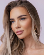 Frau mit langen, blonden Haaren und goldenen Creolen blickt zur Seite, trägt dezentes Make-up vor einem hellvioletten Hintergrund.
