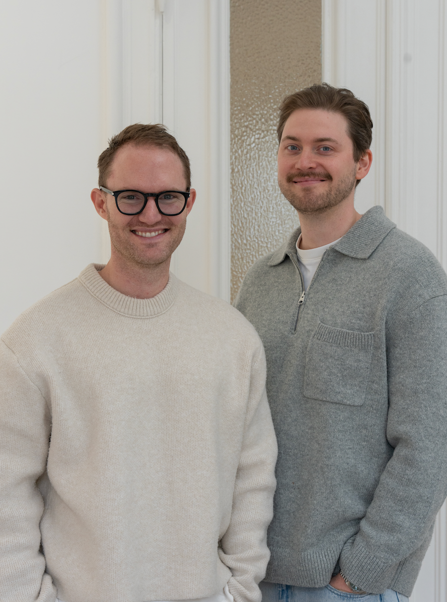 PURISH-Gründer Philipp und Lucas in hellen Strickpullovern stehen nebeneinander und lächeln in die Kamera.