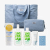 Die PURISH Sommertasche 2025 – Basic Routine besteht aus einer blauen Tragetasche mit passendem Beutel, Sonnencreme, Lotionflaschen, Gesichtscreme und einer gemusterten Karte.