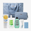 Die PURISH Summer Bag 2025 – Basic Routine enthält eine blaue Tragetasche und einen Beutel, Sonnenschutzmittel von Bondi Sands, Produkte von Fox Tan, Handcreme von Frank & Whit und eine blaue Karte.