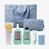 Die PURISH Summer Bag 2025 – Basic Routine enthält eine hellblaue Tragetasche, eine Kosmetiktasche, Sonnencreme, zwei Flaschen, eine Tube und eine Karte auf weißem Hintergrund.