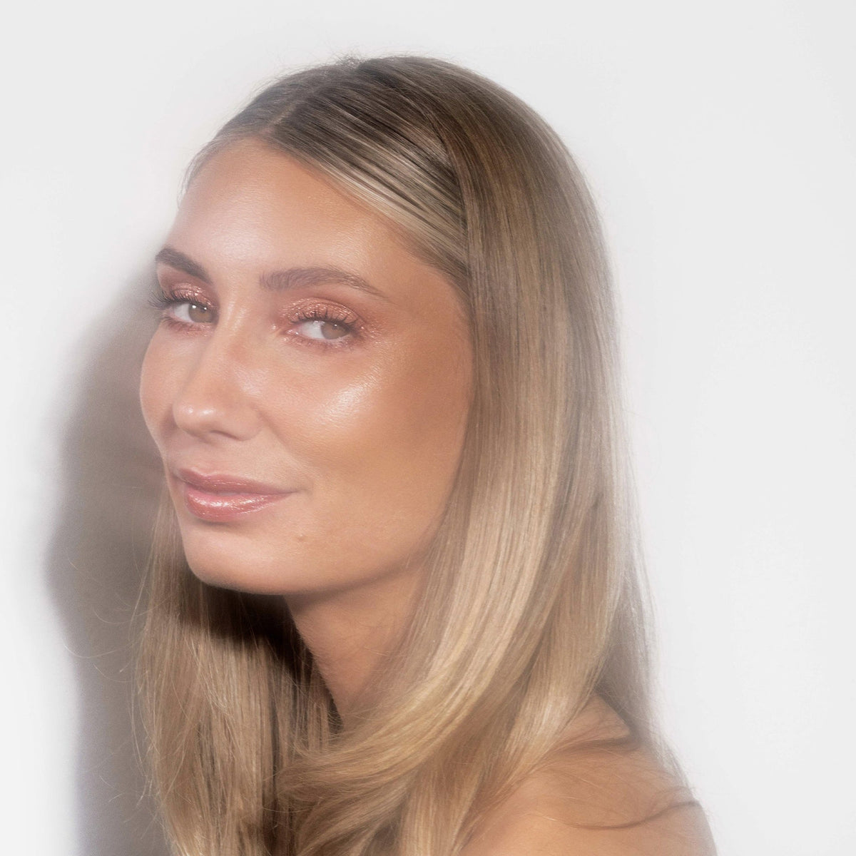 Eine Frau mit langem blondem Haar und strahlender Haut präsentiert glitzernden pfirsichdfarbenen Sparkl Flirt on LH Cosmetics.