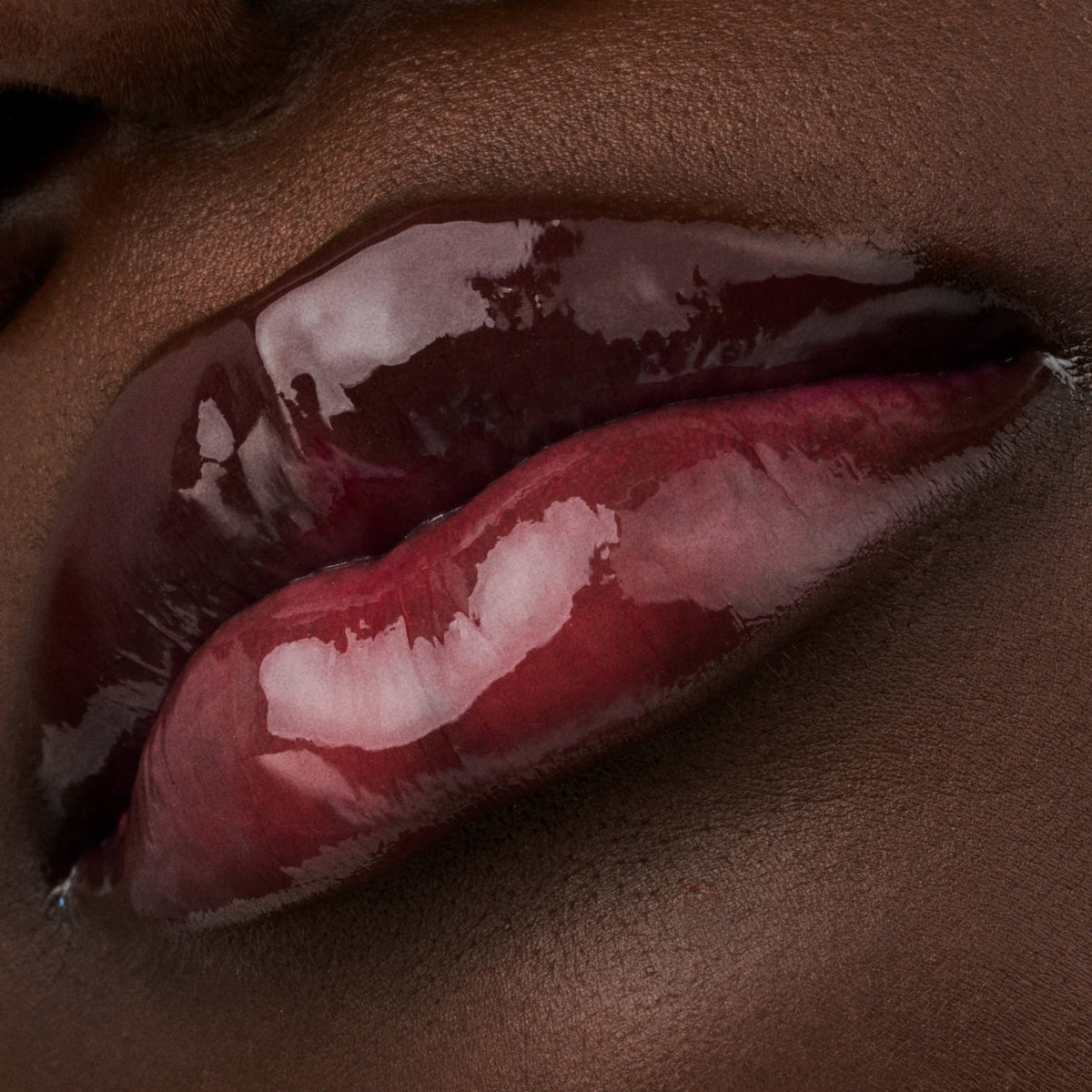 Nahaufnahme der Lippen einer Person mit dunkler Haut mit dem Glossin‘ Glow Tinted Lip Oil 010 in glänzendem transparentem Farbton.