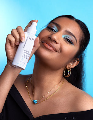 Frau mit blauem Lidschatten lächelt und hält das Liquid Hydration Spray von Geek & Gorgeous vor hellblauem Hintergrund.