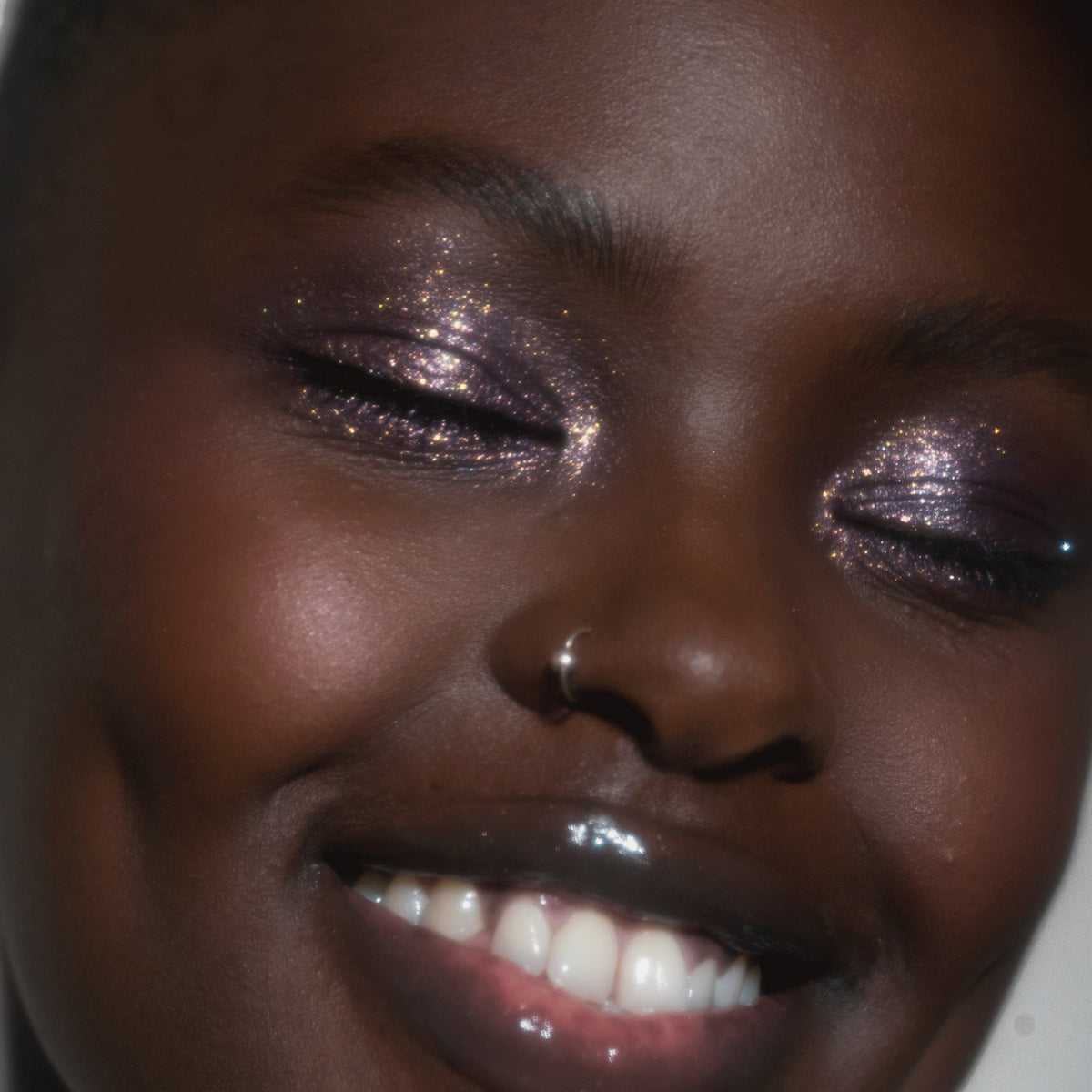 Nahaufnahme des Gesichts einer Frau  mit dunklem Hautton und lila glitzerndem Lidschatten Sparkl Magic von LH Cosmetics.