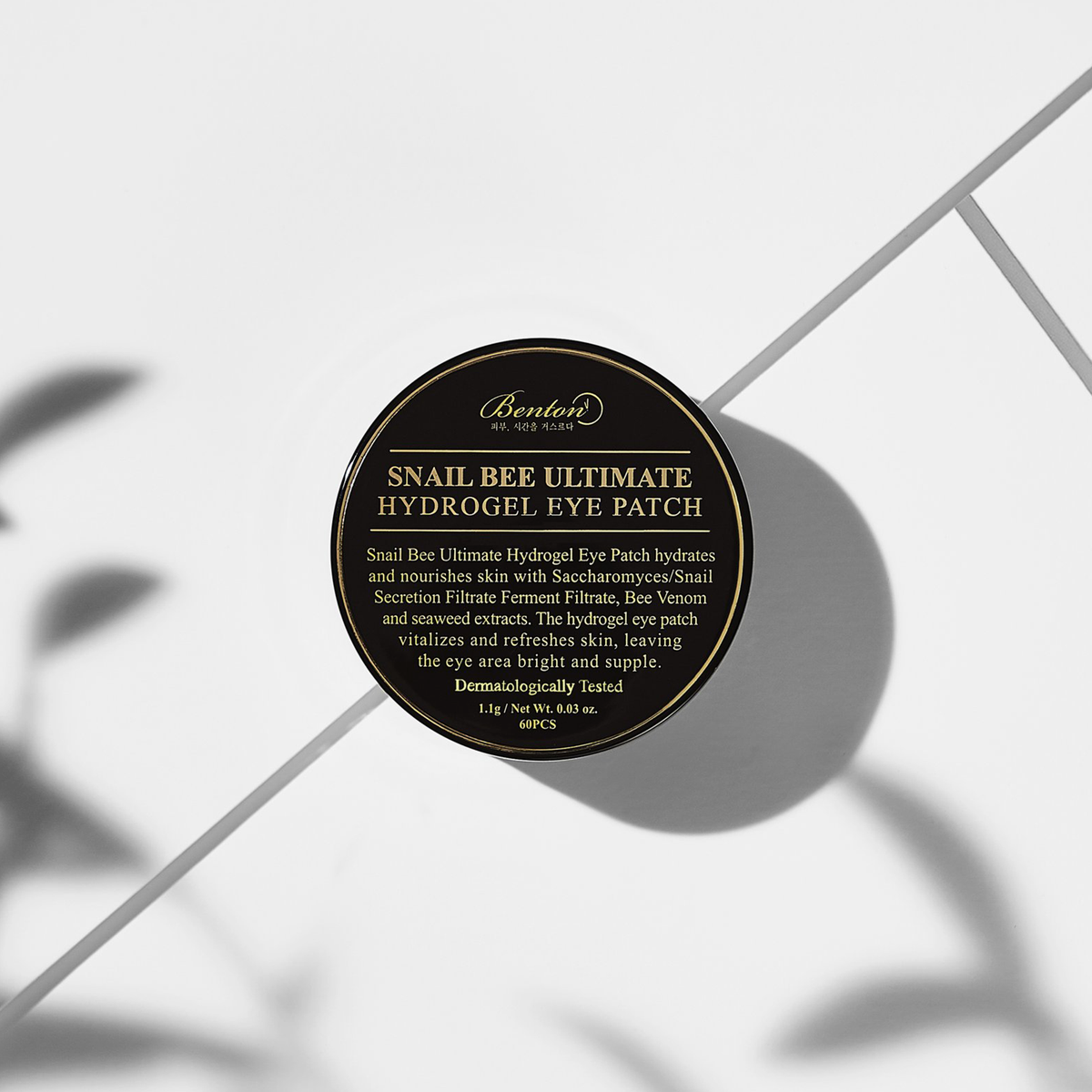 Das Snail Bee Ultimate Hydrogel Eye Patch auf weißem Fliesenboden unter dem Schatten einer Pflanze