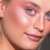 Nahaufnahme einer Person mit strahlender Haut, blauen Augen und glänzenden Lippen, die LH Cosmetics Duo Dimension Area für einen Hauch von rosa Rouge trägt.