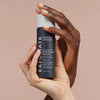Zwei Hände halten eine Flasche Skin Perfecting 2 % BHA Liquid Exfoliant vor einem beigen Hintergrund.