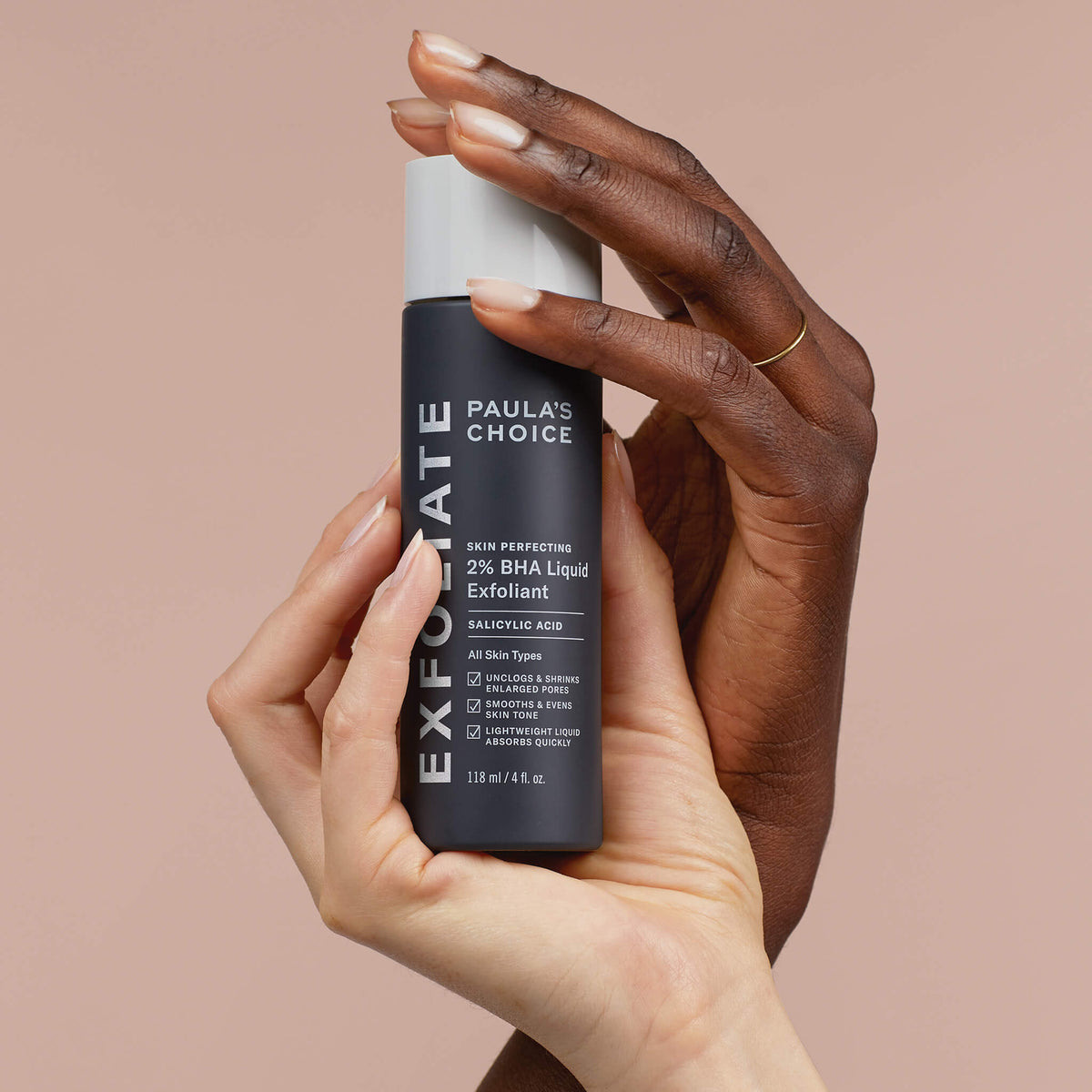 Zwei Hände halten eine Flasche Skin Perfecting 2 % BHA Liquid Exfoliant vor einem beigen Hintergrund.