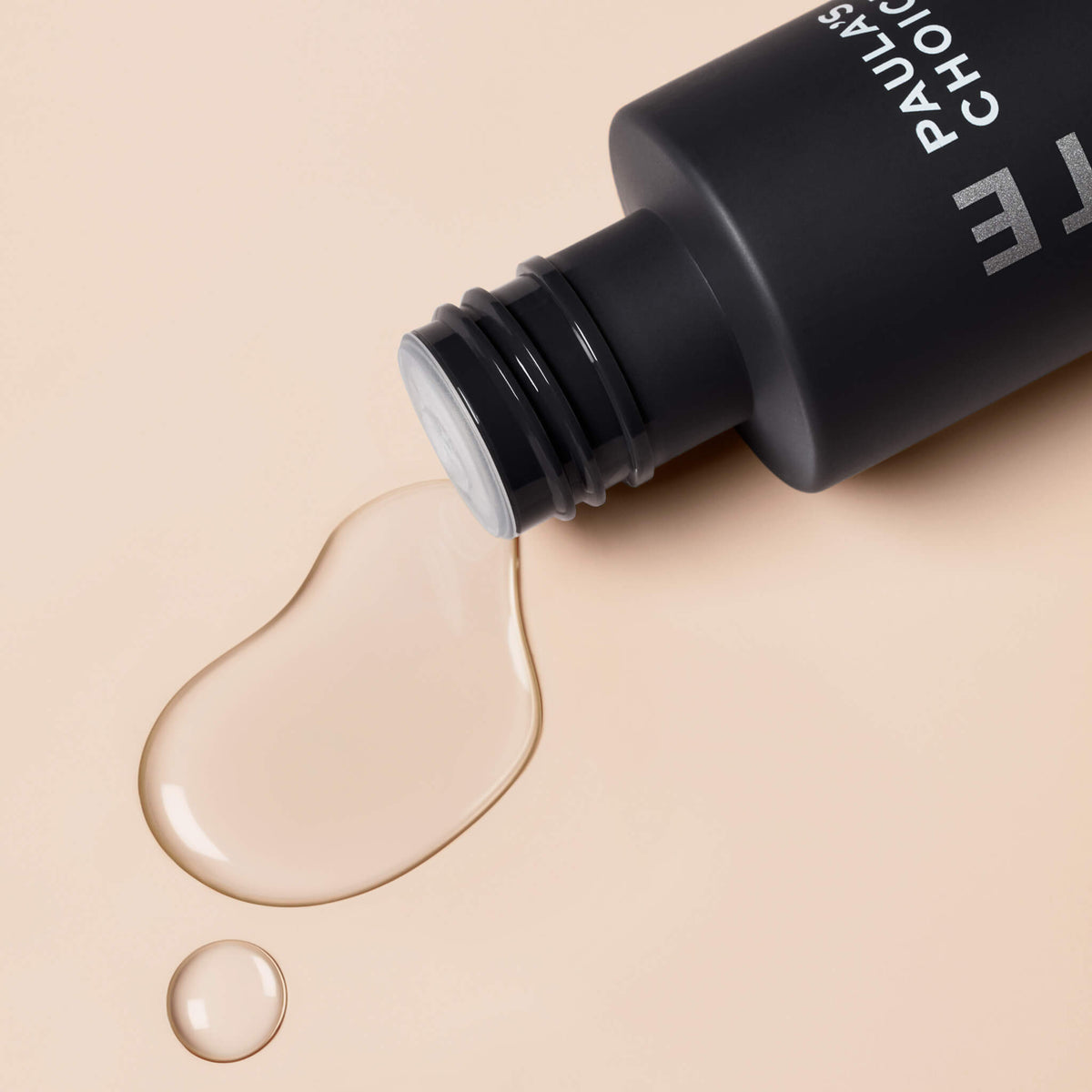 Offene schwarze Flasche Skin Perfecting 2 % BHA Liquid Exfoliant mit verschütteter Flüssigkeit auf einer beigen Oberfläche.