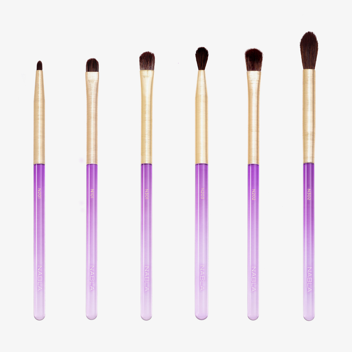 Das Amethyst Detail Brush Set enthält sechs Make-up-Pinsel mit goldenen Zwingen und violetten Farbverlaufsgriffen, die in einer Reihe auf weißem Hintergrund angeordnet sind.