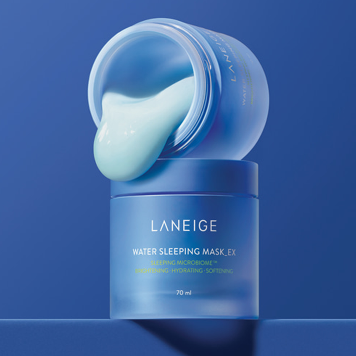 Offenes Glas der Laneige Water Sleeping Mask Ex, aus der vor blauem Hintergrund hellblaue Creme herausquillt, steht auf weiterem Tiegel.