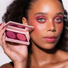 Eine Frau mit kräftigem rosa Augen- und Wangen-Make-up hält die LH Cosmetics Duo Dimension Element Palette mit zwei Farbtönen in die Nähe ihres Gesichts.
