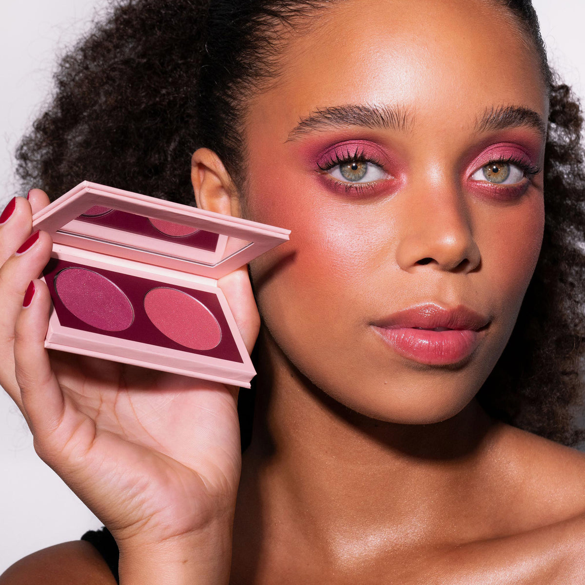 Eine Frau mit kräftigem rosa Augen- und Wangen-Make-up hält die LH Cosmetics Duo Dimension Element Palette mit zwei Farbtönen in die Nähe ihres Gesichts.