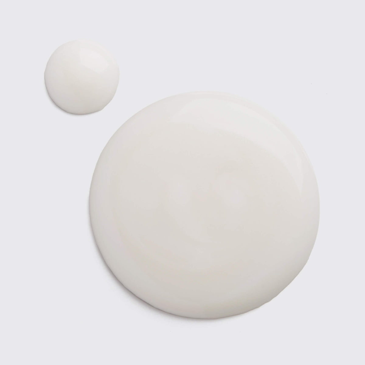 Zwei elfenbeinfarbene Tropfen Discoloration Repair Serum, einer groß und einer kleiner, auf weißem Untergrund.