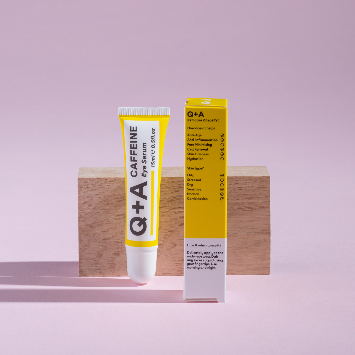 Die Tube und Schachtel präsentiert vor einem Holzblock vor rosa Hintergrund.