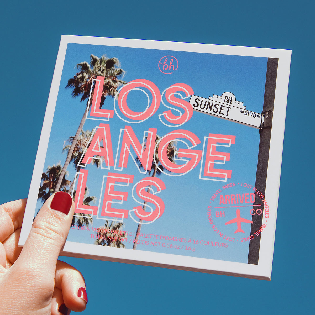 Hand mit roten Nägeln hält die Lost in Los Angeles 16 Color Shadow Palette in Richtung eines blauen Himmels