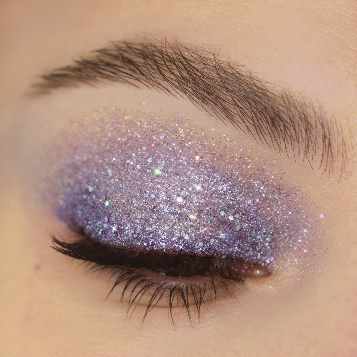 Geschlossenes Auge mit schimmerndem lila und silbernem Lidschatten aus der Miami Lights Glitter Palette, kombiniert mit langen dunklen Wimpern.