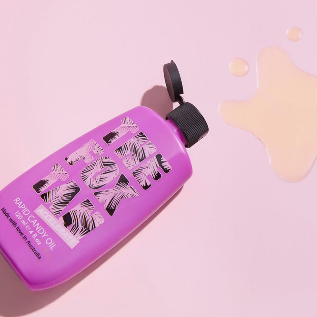 Eine violette Flasche Rapid Candy Oil steht auf einer rosa Oberfläche, um die herum etwas Öl verschüttet ist.