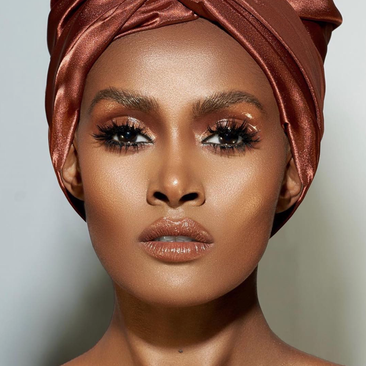 Eine Frau mit strahlend brauner Haut, dramatischem Make-up aus der Waterproof Cream Palette und einem glänzenden bronzenen Kopftuch blickt selbstbewusst geradeaus.