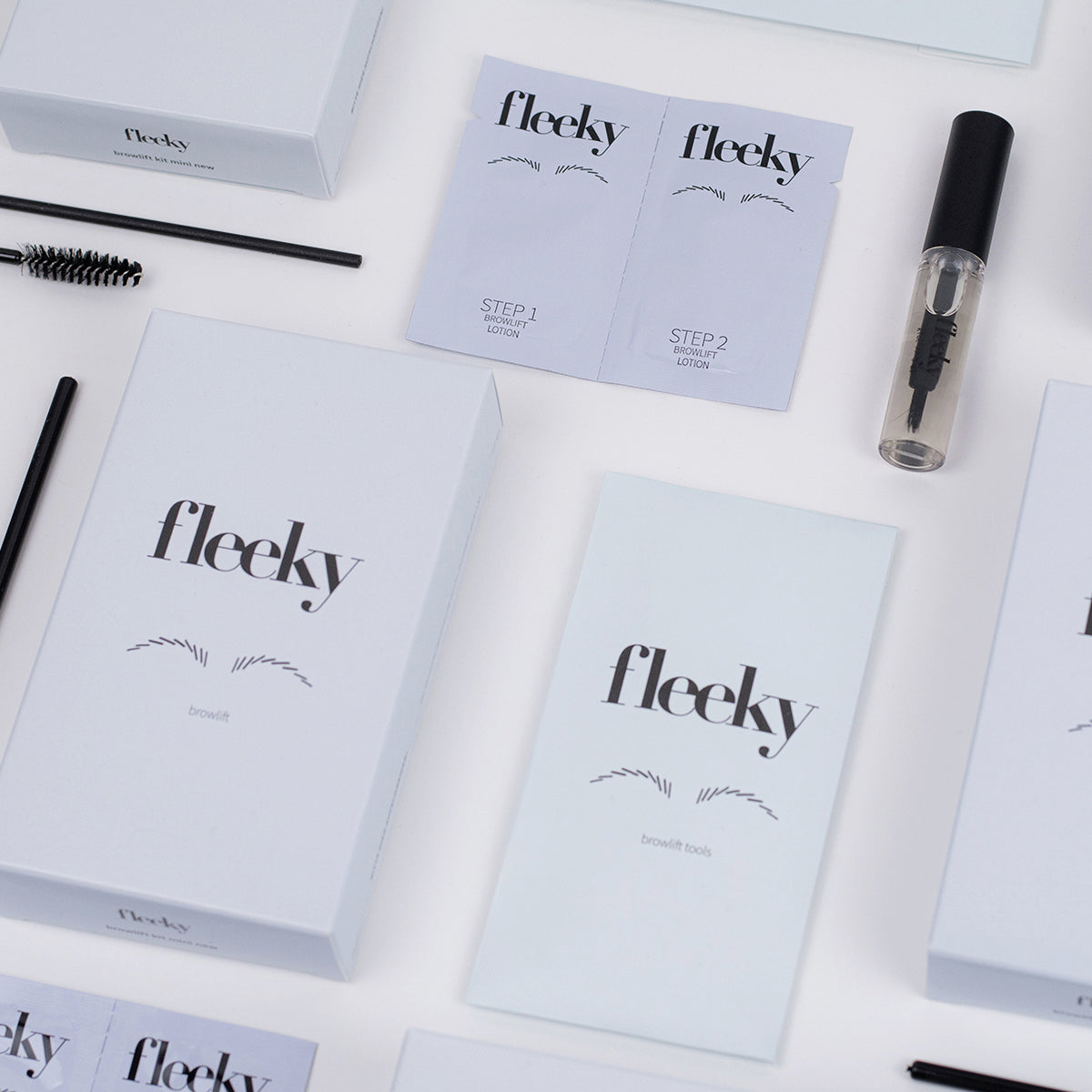 Das Browlift Kit Mini inklusive Boxen, Lotions, Brauenbürsten auf einer weißen Fläche angeordnet.