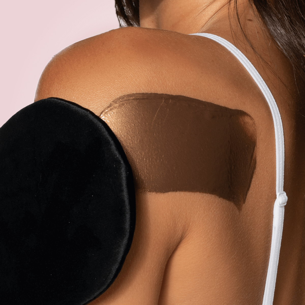 Eine Frau trägt mit einem Bräunungshandschuh die Loving Tan Bronze Shimmer Luminous Cream auf ihre Schulter auf.