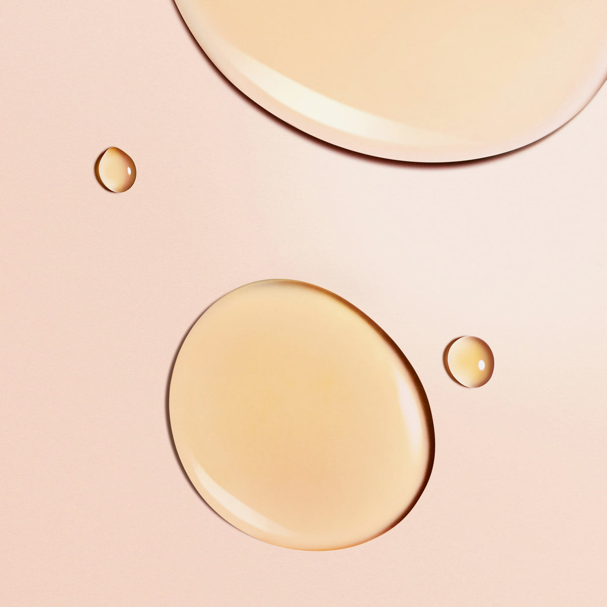 Nahaufnahme der beigen Tröpfchen der Honey Lip Care Rêve de Miel von NUXE auf einer glatten, blassrosa Oberfläche.