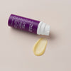 Eine violette Flasche „Clinical 1 % Retinol Treatment“ von Paula’s Choice mit Pumpe liegt neben einem Klecks gelblicher Creme auf einem hellen Hintergrund.