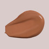 Ein Klecks Wide Awake Full Coverage Concealer Cafe de Canela in Warmbraun auf einem blassen Hintergrund.