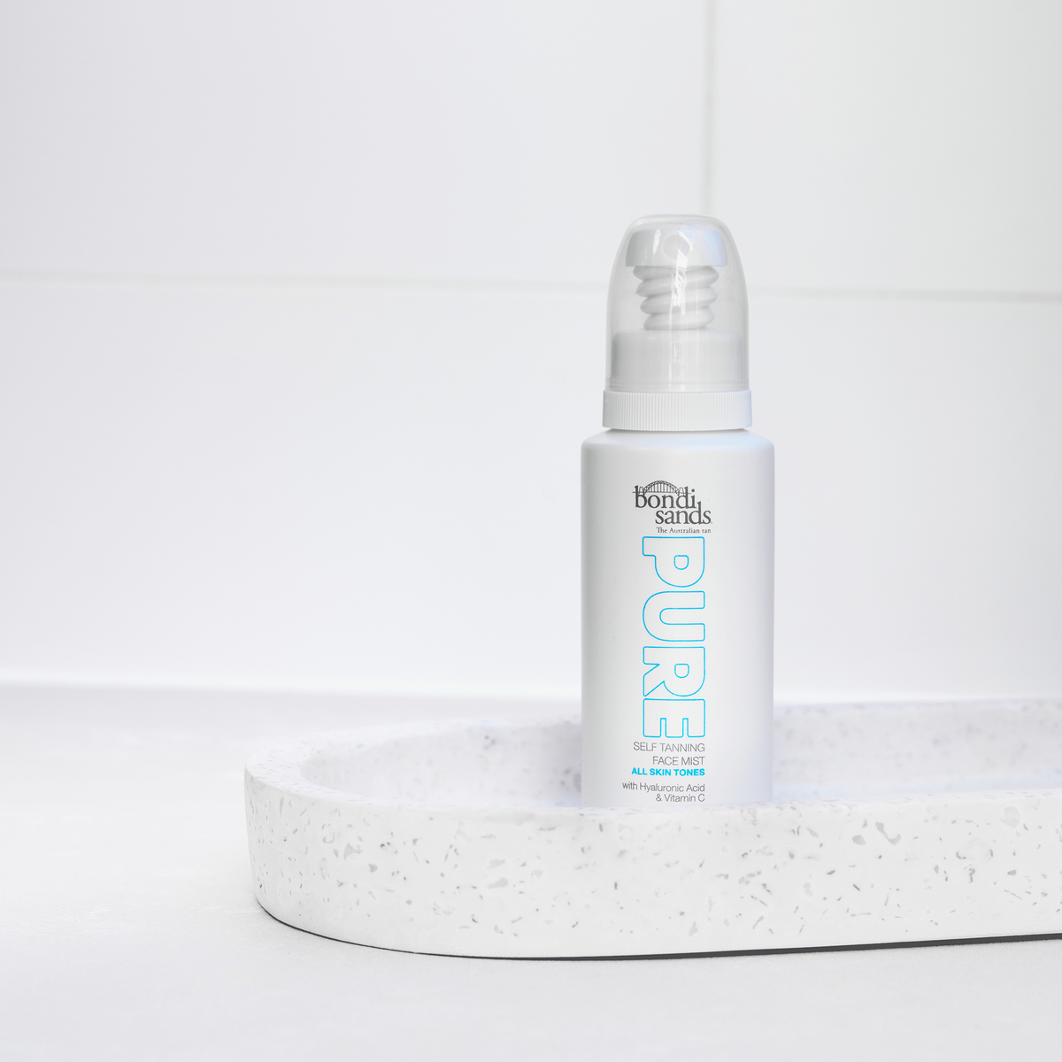 Eine Flasche Pure Tanning Face Mist von Bondi Sands steht auf einem gesprenkelten weißen Tablett in minimalistischem Ambiente